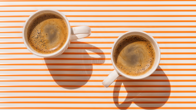 Two white espresso cups filled with espresso on an orange and white striped background.