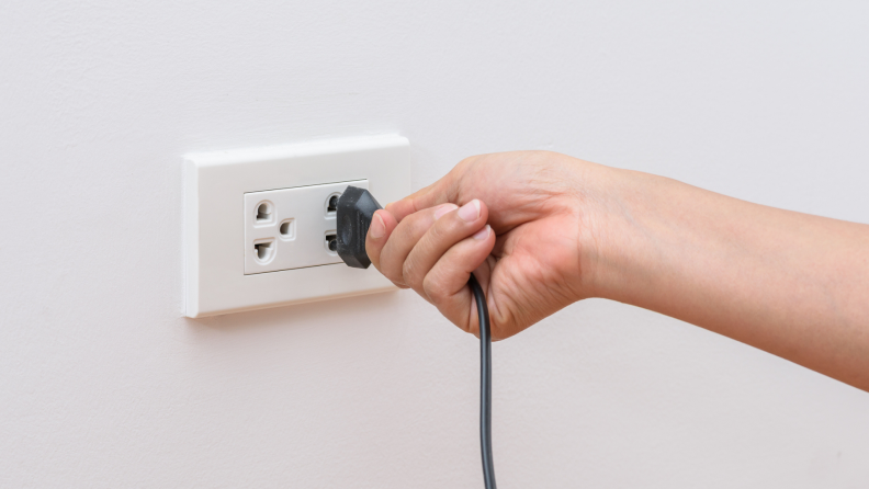 Person unplugging plug from electrical outlet