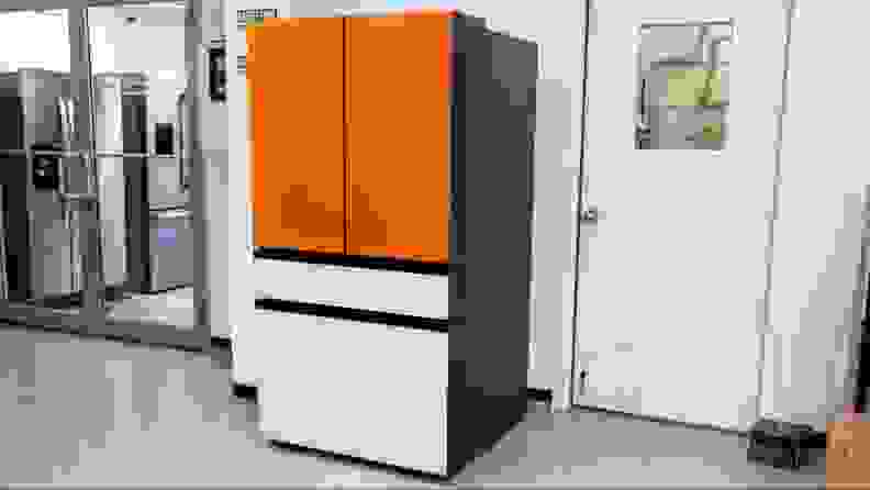A shot of a Samsung Bespoke French-door sitting outside our fridge testing lab. The top two panels are bright orange and the flex drawer and freezer panels are white.