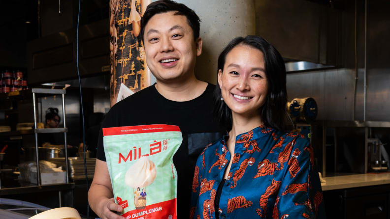 Jen and Caleb posing together, holding a bag of Mila dumplings