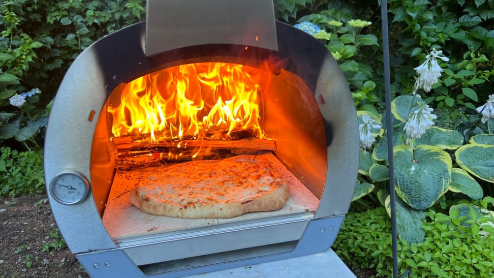 The Cru 32 pizza oven sitting outside, with a fire and pizza cooking inside.