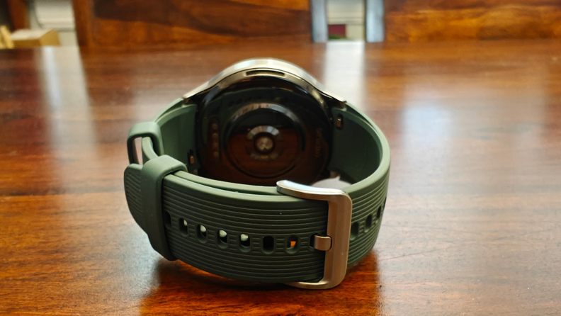 Close-up view of the back of a clasped OnePlus Watch 2 resting on a brown table surface.