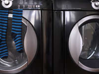 A close-up of a dark navy blue washer and dryer pair. A pair of blue and black striped socks hang from the door of the washer.