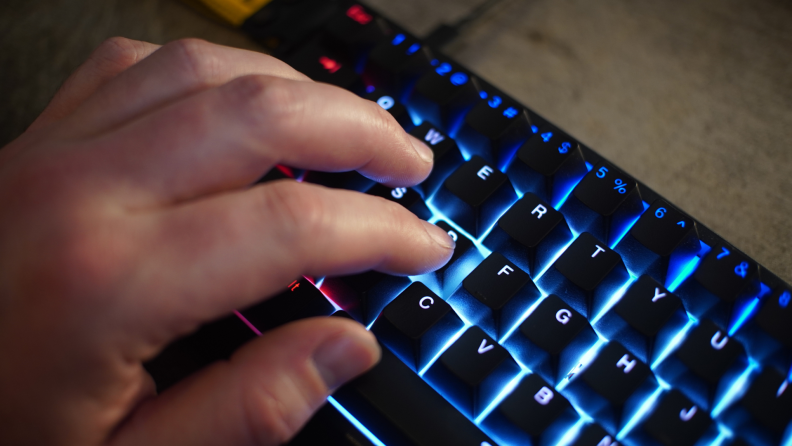 Close up angled shot of someone resting their hand on the Wooting 60he keyboard with rainbow backlit display turned on.