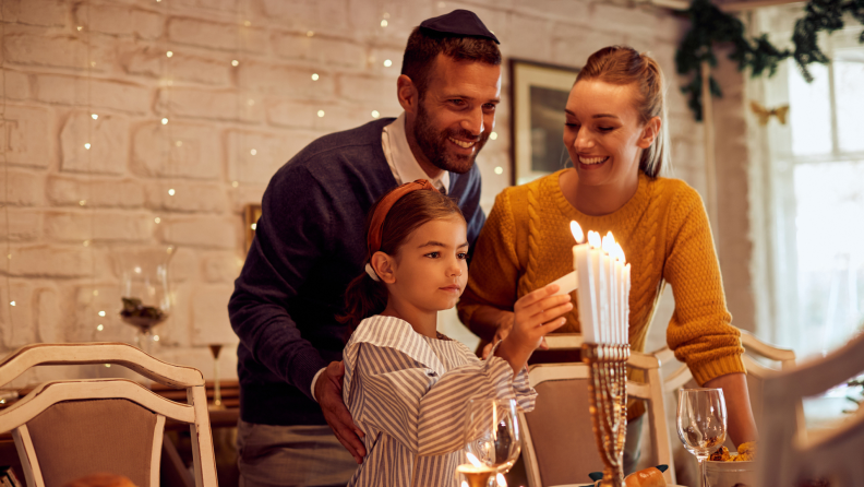 Family of three lighting candle on menorah in celebration of jewish holiday.