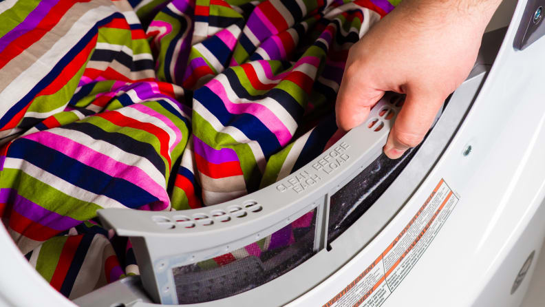 A hand reaches in from out of frame to remove the Whirlpool WED6620HW dryer's lint trap. A colorful blanket is in the drum for scale.