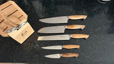 Five Cangshan knives laid out on black countertop beside the wooden knife block.