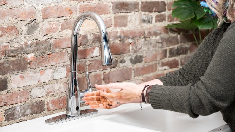 A person washes dirty hands in front of a kitchen faucet