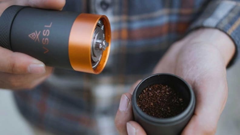 A person is holding a VSSL Java coffee grinder.
