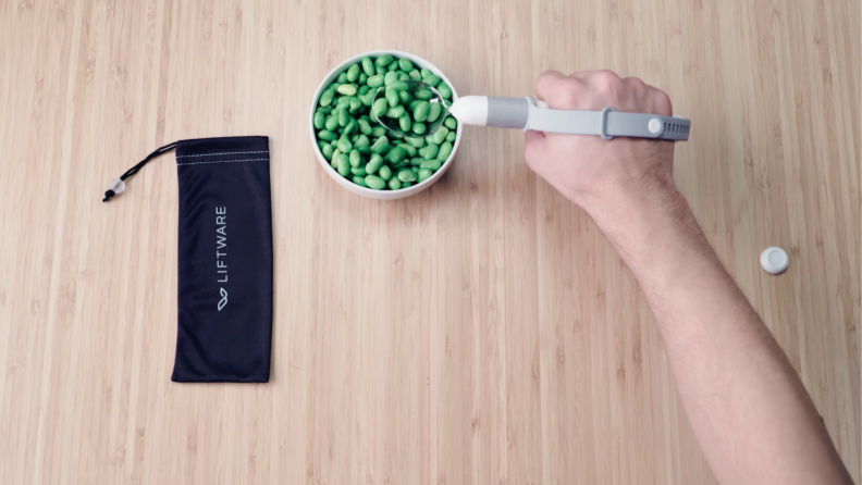 Person using liftware spoon to pick up green beans in bowl.