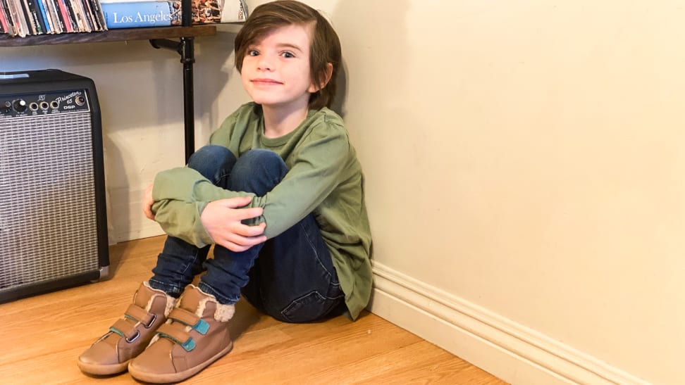 A smiling child wearing brown high top sneakers.