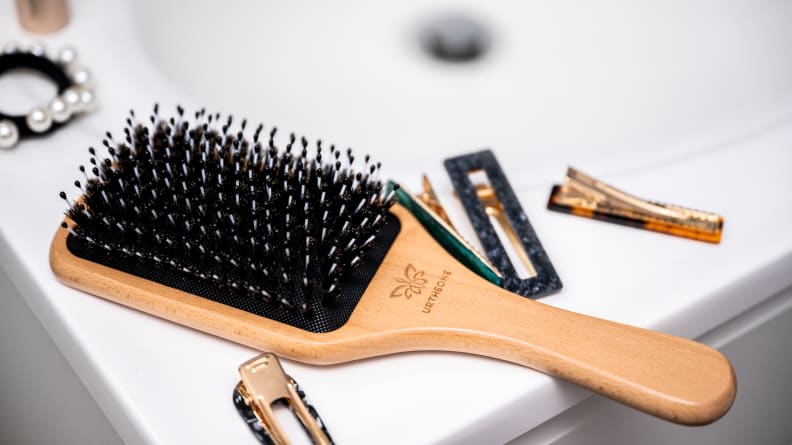 A wooden paddle brush laying on the bathroom sink with hair clips around it.