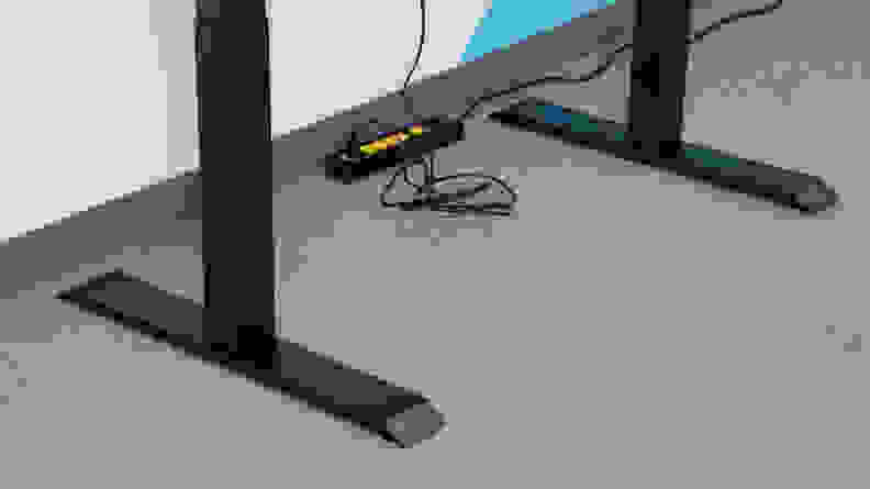 Close-up of the standing desk's power cords and feet on a gray floor.