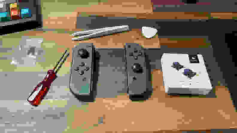 A picture of the Nintendo Switch joycons along with some tools to disassemble it, as well as an extra pair of joysticks by GuliKit.