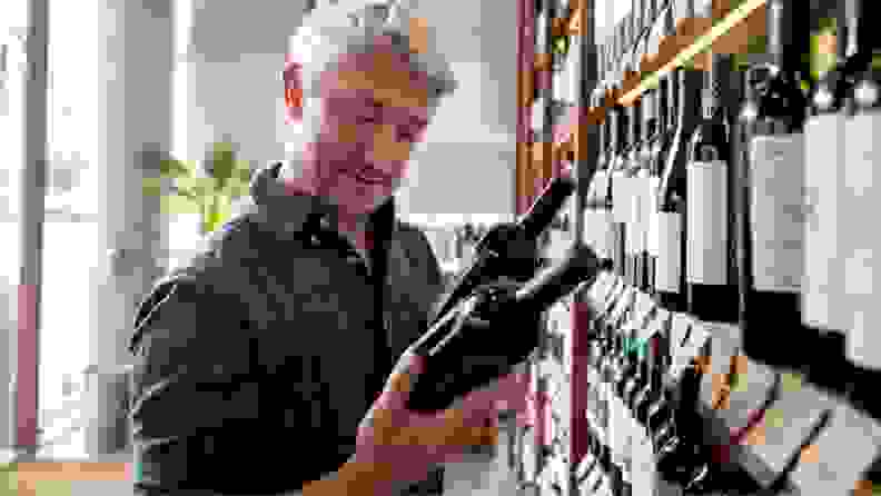 A man reads the label on a bottle of wine as he peruses a wine store's shelves