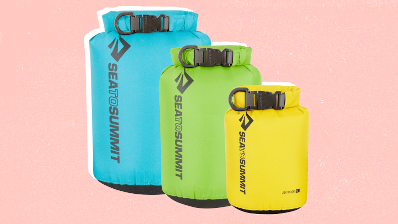 A large blue dry bag, a green medium dry bag, and a yellow small dry bag against a pink background.