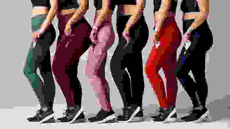 Six women in leggings standing sideways in a line, putting phones in their legging pockets.