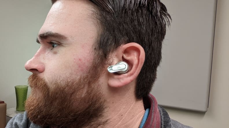 The profile of a man with a beard and the JBL Tour Pro 2 earbuds in his ear.