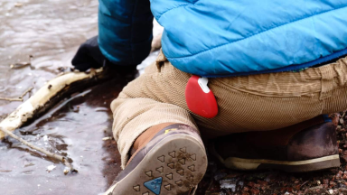 A child wearing a red GPS tracker on a belt loop kneels on the ground.