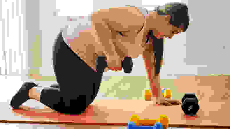 A woman using dumbbells on a yoga mat.