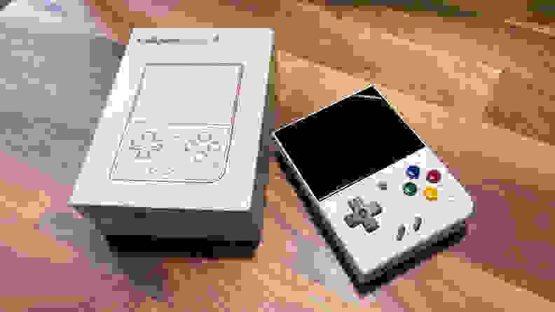 The Miyoo Mini Plus handheld console laid on a tabletop next to its beige, retro packaging.