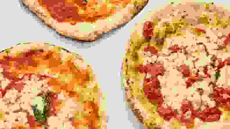 A top down photo of three pizzas against a white surface.