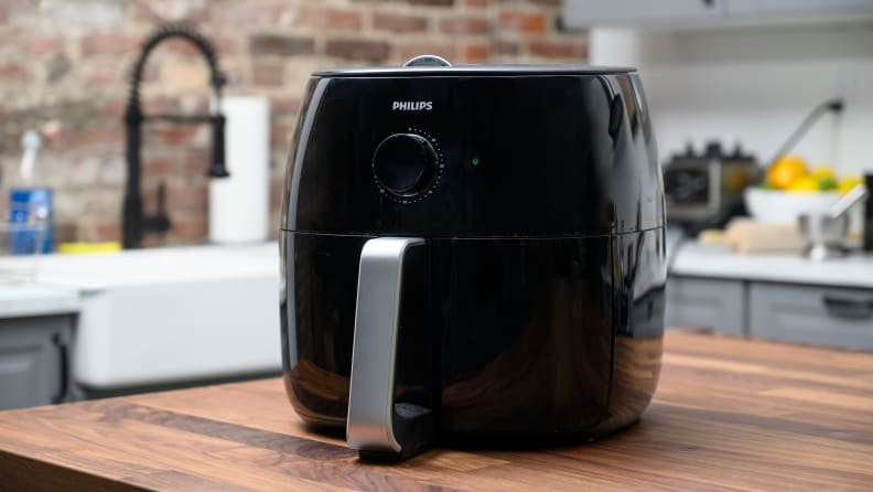 The Philips XXL air fryer sits on a kitchen counter. It has a silver handle in front of the black appliance.