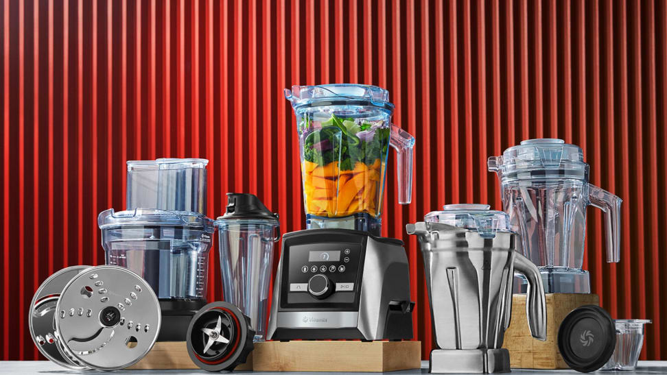 Several Vitamix blenders and accessories in front of a red backdrop