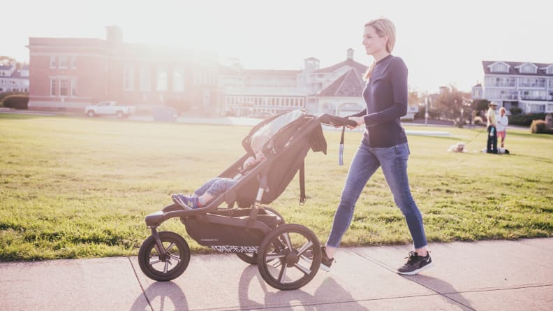 A woman pushing a jogging stroller with a child riding inside.