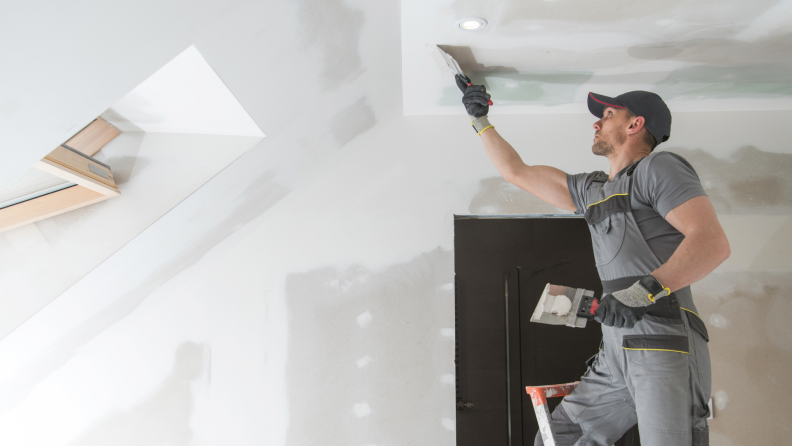 man plasters over blue board on a new ceiling