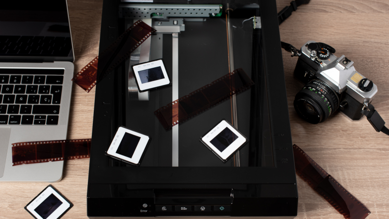 A retro 35mm camera, transparencies, negatives, and a scanner as part of a digitization process.