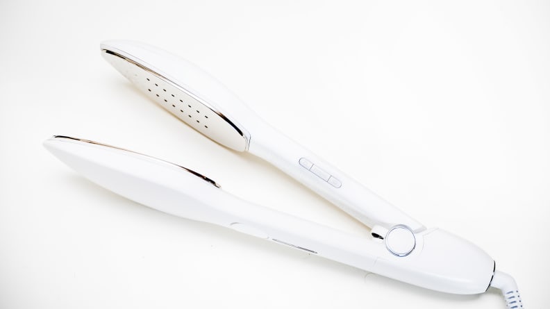 A travel iron that resembles a hair straightener rests on a surface