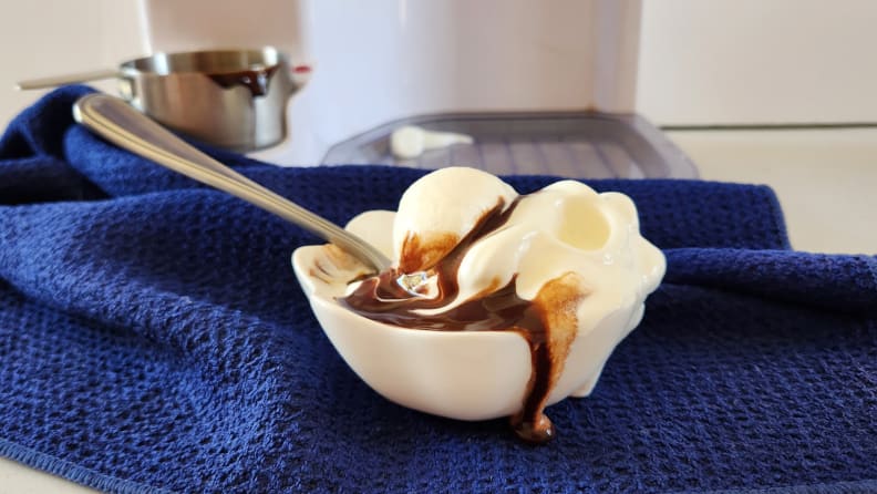 Ice cream sundae with chocolate sauce inside of small dish with spoon on top of blue dish towel.