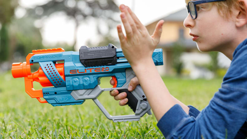 A boy, laying in the grass, aiming a a nerf gun