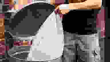 A person putting a trash bag inside of a garbage can.