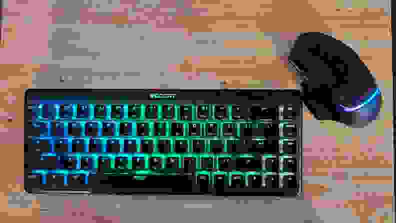 Roccat Vulcan II Mini Air keyboard with colorful LED backlit display next to computer mouse resting on top of hardwood surface.