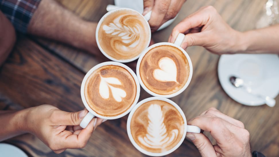 Four people holding cups of cappuccino from above,  displaying cappuccino art