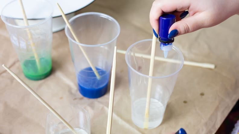 A hand dropping blue color pigment into a cup containing resin