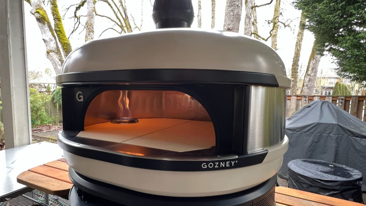 Gozney Dome Pizza Oven outdoors on stand with wood side table.
