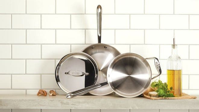 Three pots and pans against a tiled kitchen wall.