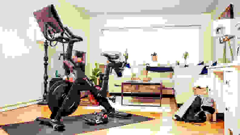 Peloton exercise bike on top of workout mat inside of living room surrounded by furniture.