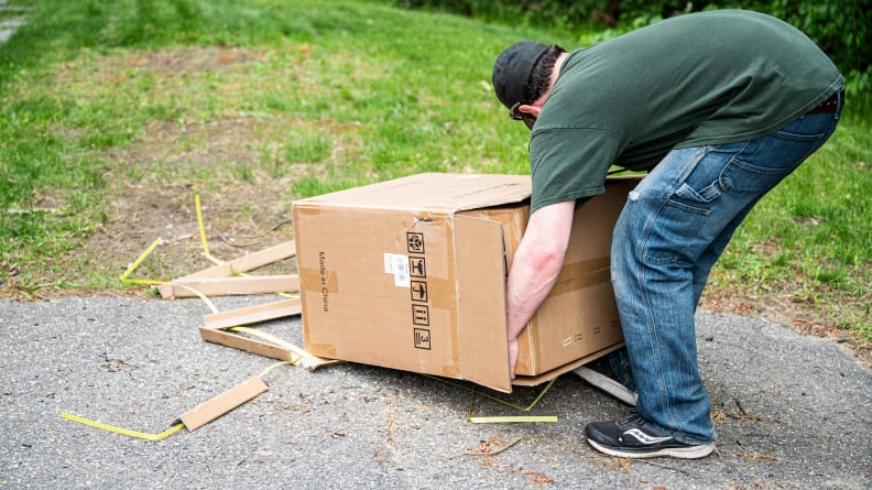A person lifts a generator out of a cardboard box outside.