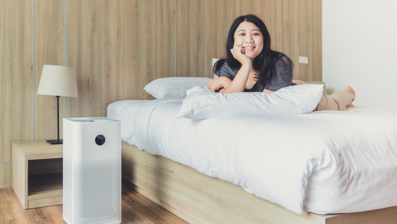 Person laying on mattress smiling next to air quality monitor.
