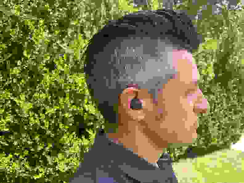 A man in a blue shirt with the Sony LinkBuds S in his ear stands in profile in front of a bush.