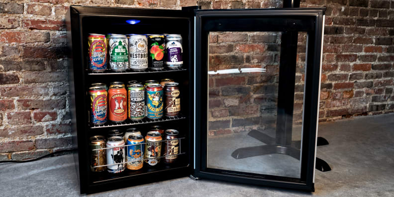 The Wine Enthusiast Evolution Series Beverage Center, sitting against a brick wall with its door open, showcasing a bunch of beer inside.