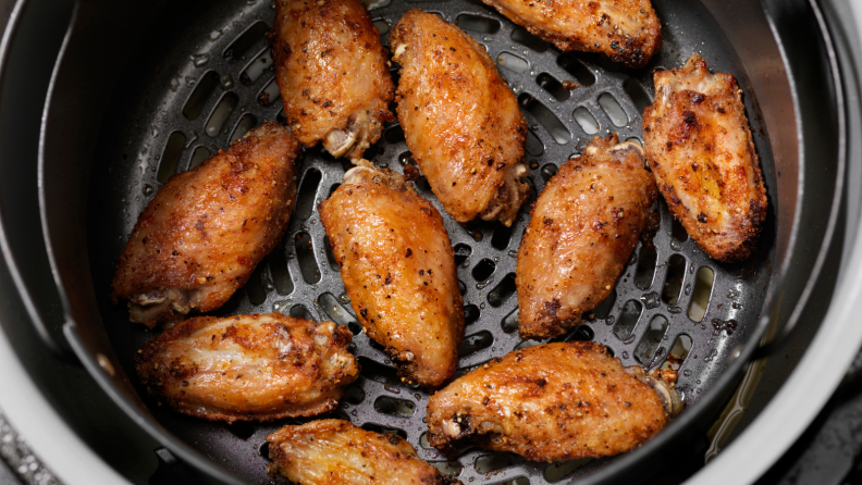 Shot from above of an air fryer basket with cooked chicken wings inside.