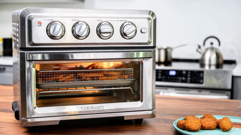 Духовка Cuisinart Air Fryer Toaster Oven представляет собой серебристый прибор с четырьмя ручками наверху и несколькими полками внутри.