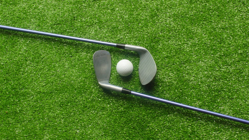 Two golf clubs and a golf ball on a putting green
