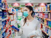 A woman, wearing a face mask, is in the cleaning product aisle of a store, comparing two different options.
