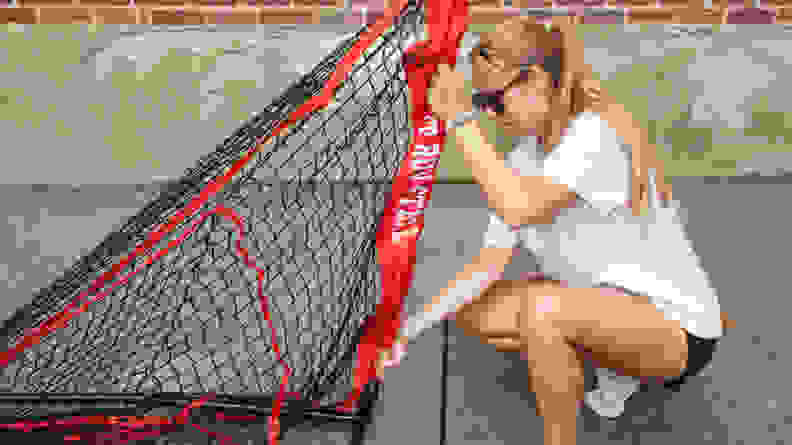 Person crouching down to disassemble hitting net outdoors in front of brick wall.